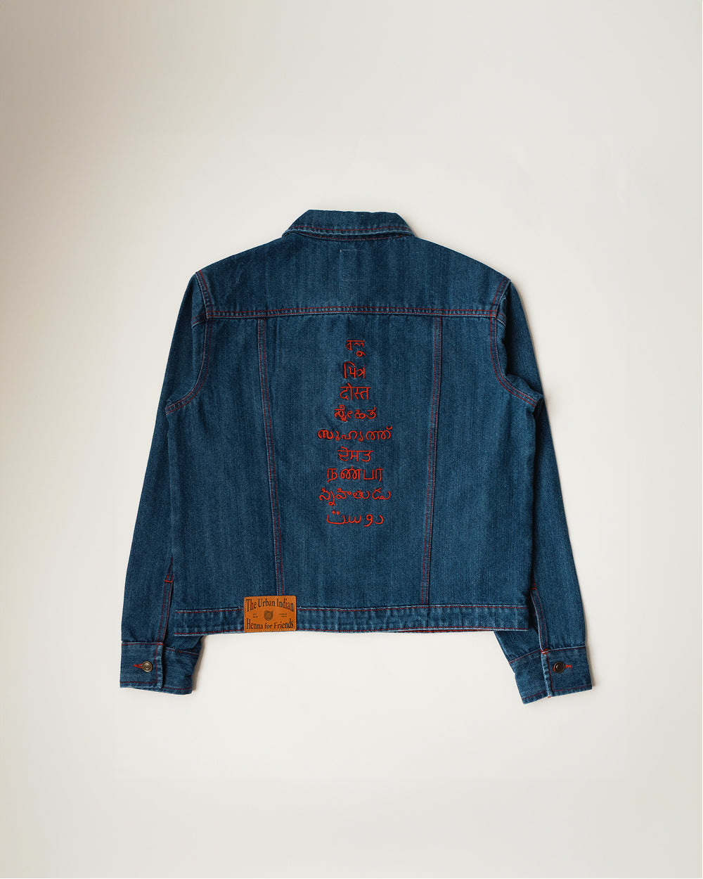 Back of the Khadi denim jacket in Medium Blue, friend embroidered down the centre in nine languages in red thread, leather patch at the hem