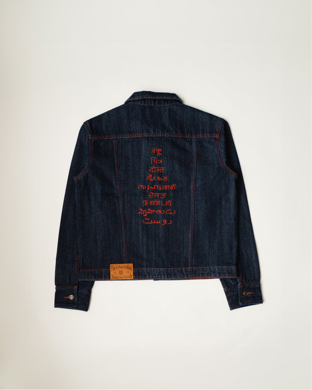 Back of the Khadi denim jacket in Raw Indigo, friend embroidered down the centre in nine languages in red thread against dark indigo