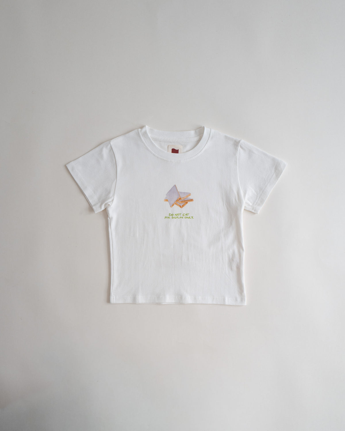 Sweets Baby Tee in Kaju Katli, flat lay, white with a small watercolor kaju katli on the chest #Color_Kaju Katli