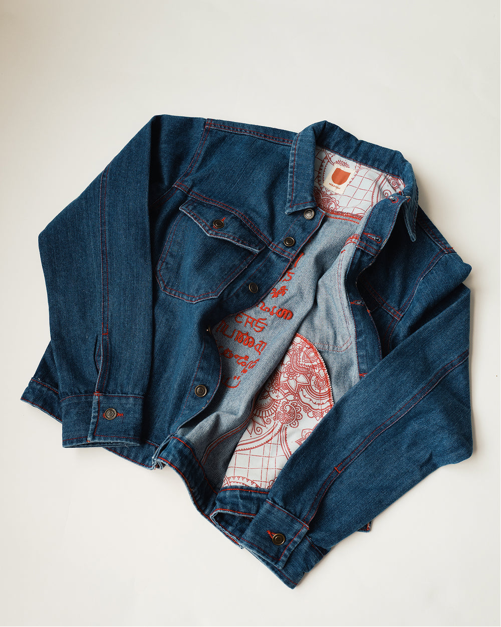 Khadi denim jacket in Medium Blue laid open to show the henna print lining in red on cream inside the placket