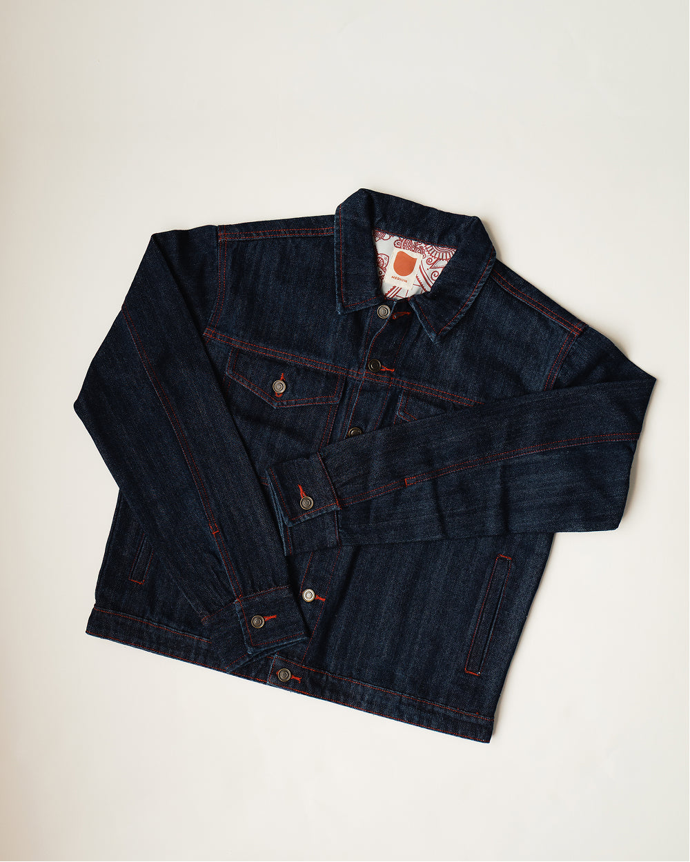 Khadi denim jacket in Raw Indigo folded flat, front view with the henna print lining showing at the collar