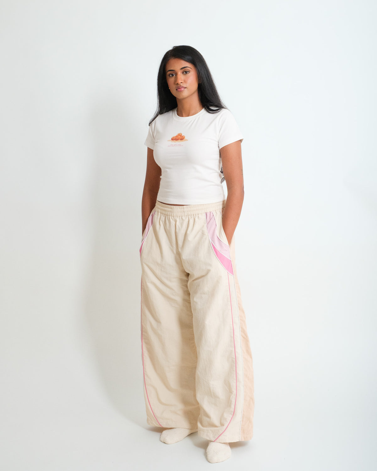 Woman in the Sweets Baby Tee in Gulab Jamun and the Sweets Track Pants in Rose Pink, hands in pockets #Color_Rose Pink