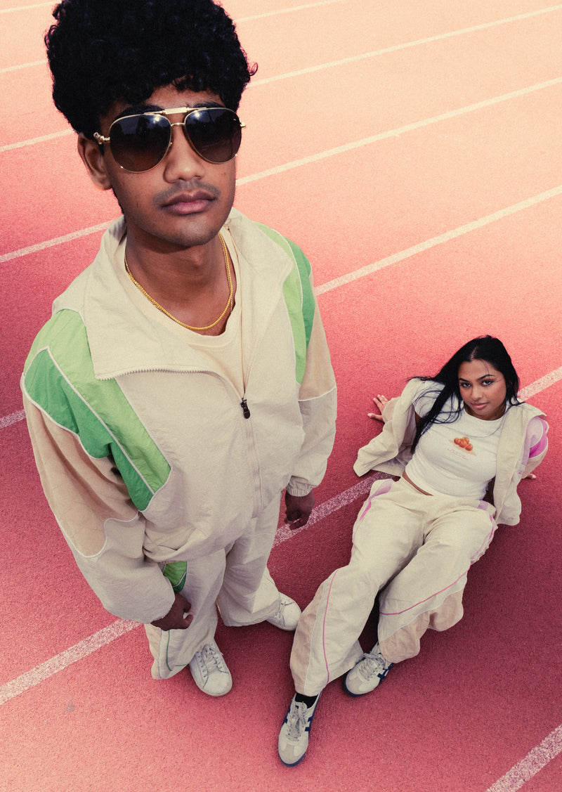 Two friends on a red running track in the Sweets Track Set, one standing in Pista Green and one lying back in Rose Pink