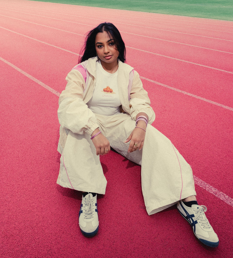 Woman sitting on a red running track in the Rose Pink Sweets Track Set and the Gulab Jamun Baby Tee