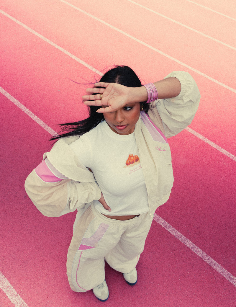Woman shading her eyes on a red running track in the Rose Pink Sweets Track Set and the Gulab Jamun Baby Tee