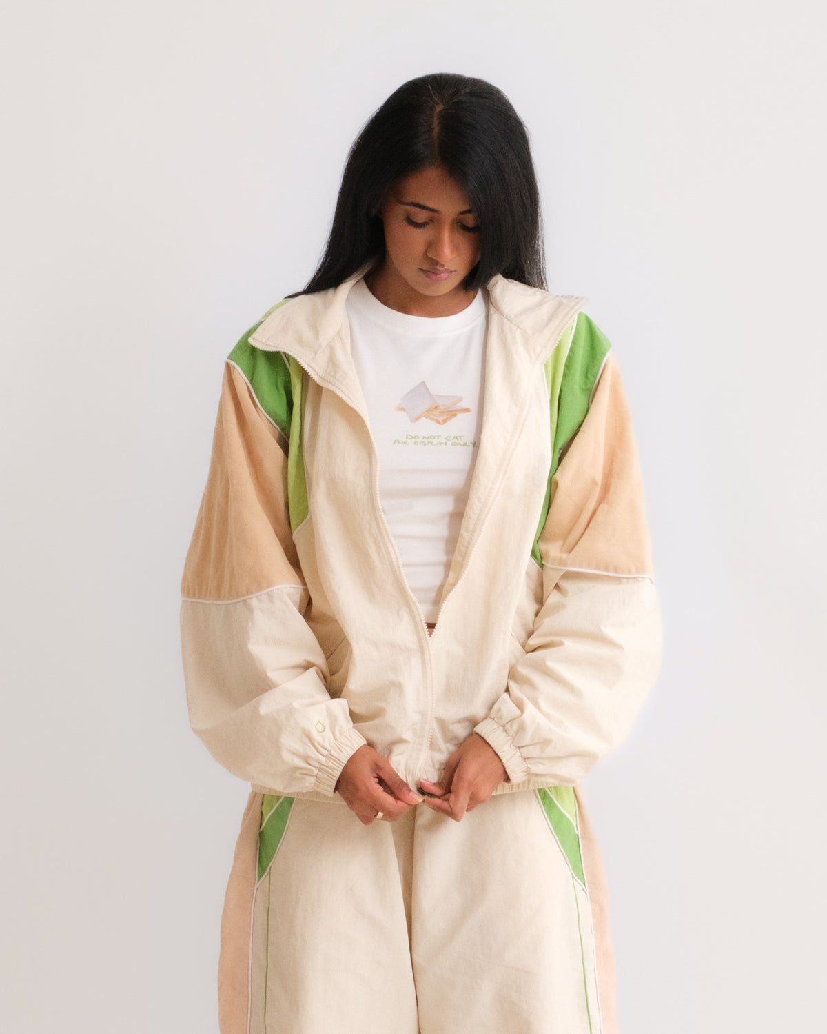 Woman zipping up the Sweets Track Jacket in Pista Green over the Kaju Katli Baby Tee, with the matching Track Pants #Color_Pista Green