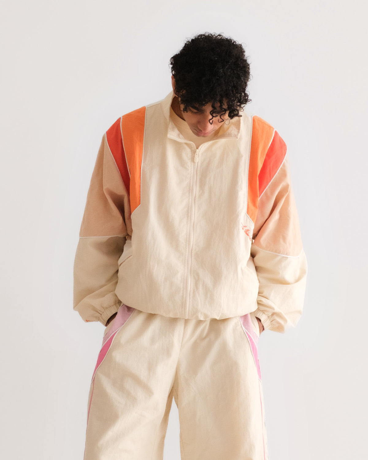 Man in the Sweets Track Jacket in Saffron Orange, felt shoulder patch and piped contrast stripes, with the Sweets Track Pants in Rose Pink #Color_Saffron Orange