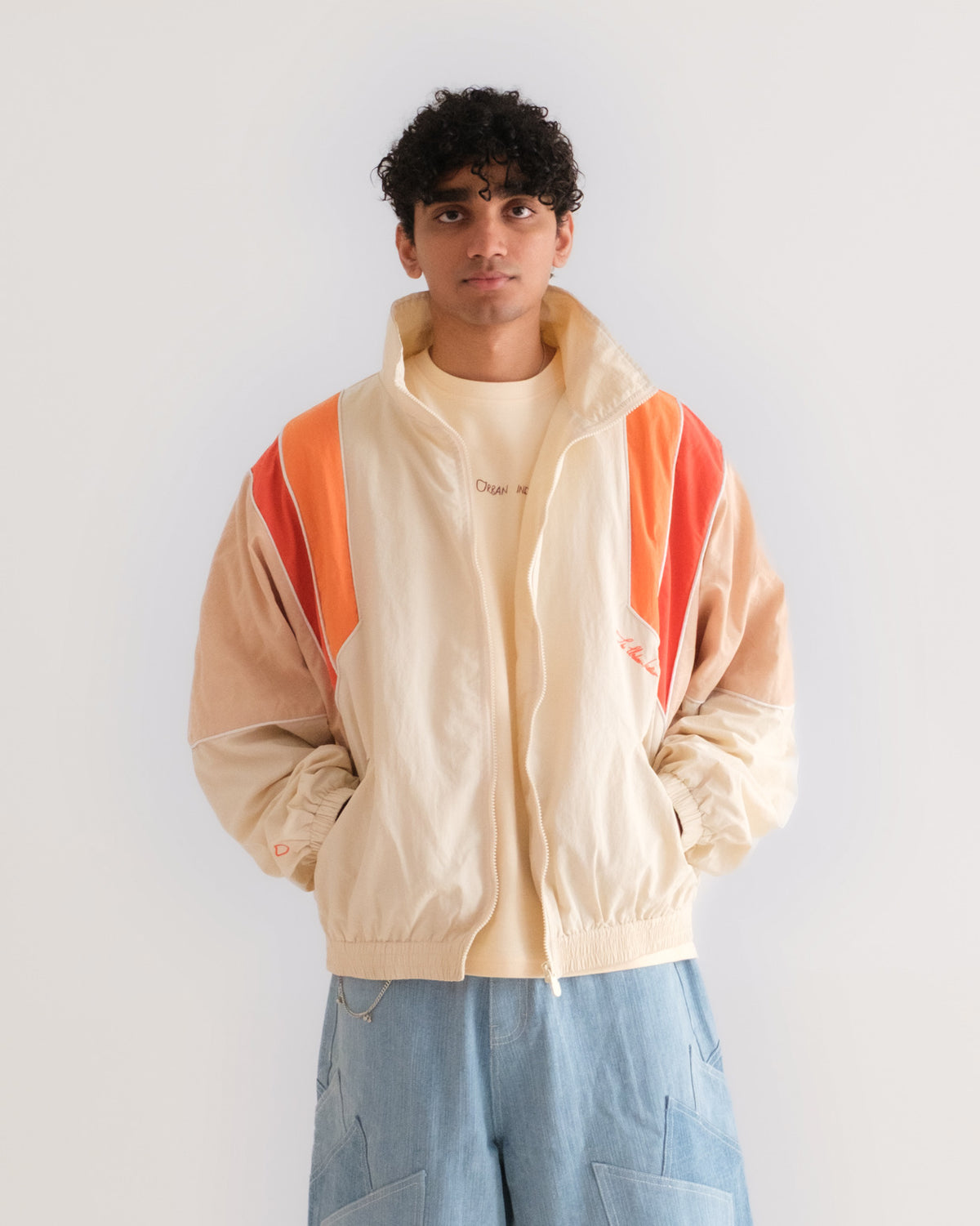 Man wearing the Sweets Track Jacket in Saffron Orange open over the Recipe Tee, with the Khadi Katli Jorts #Color_Saffron Orange