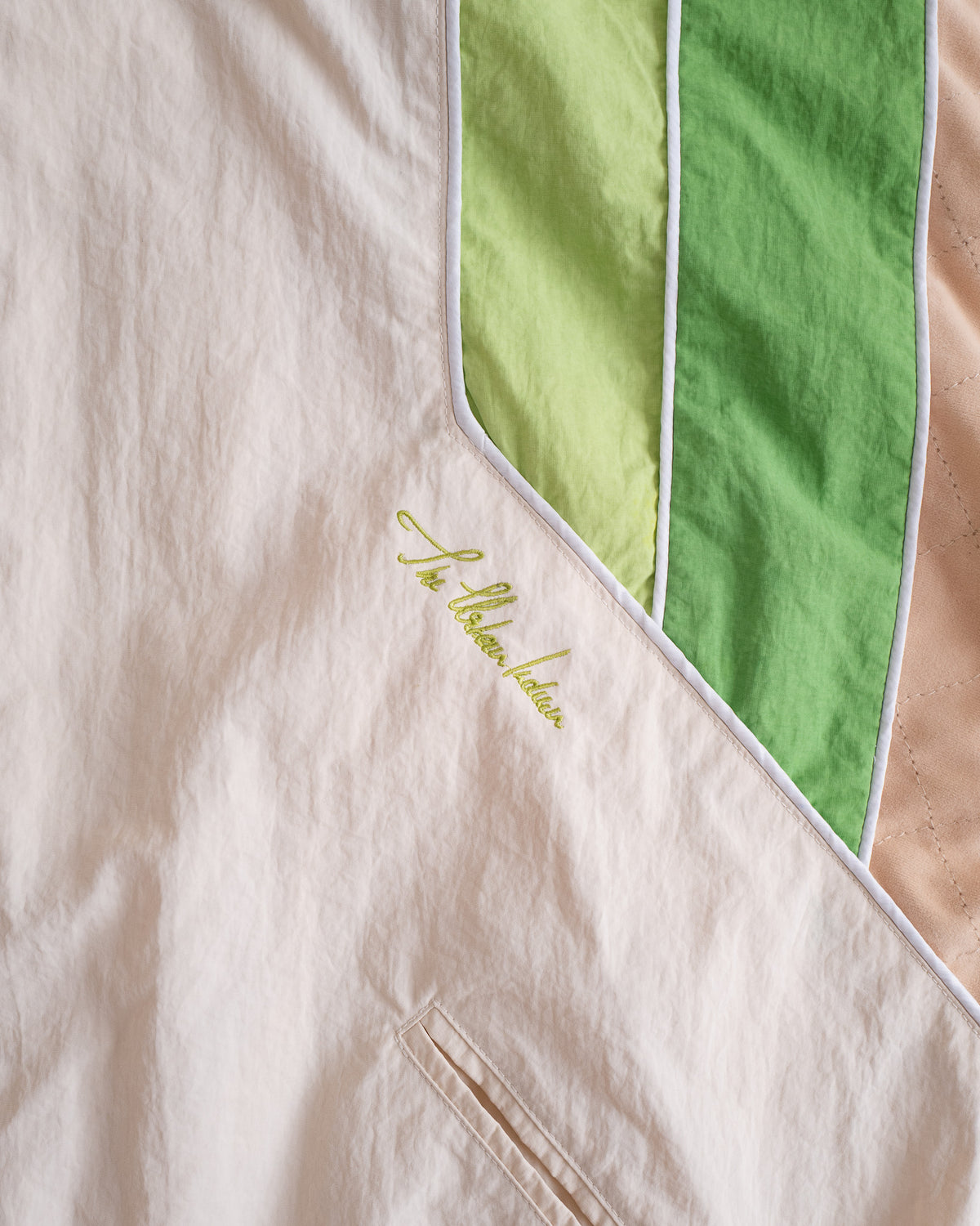 Close-up of the Pista Green stripes, white piping and embroidered script on the Sweets Track Jacket #Color_Pista Green