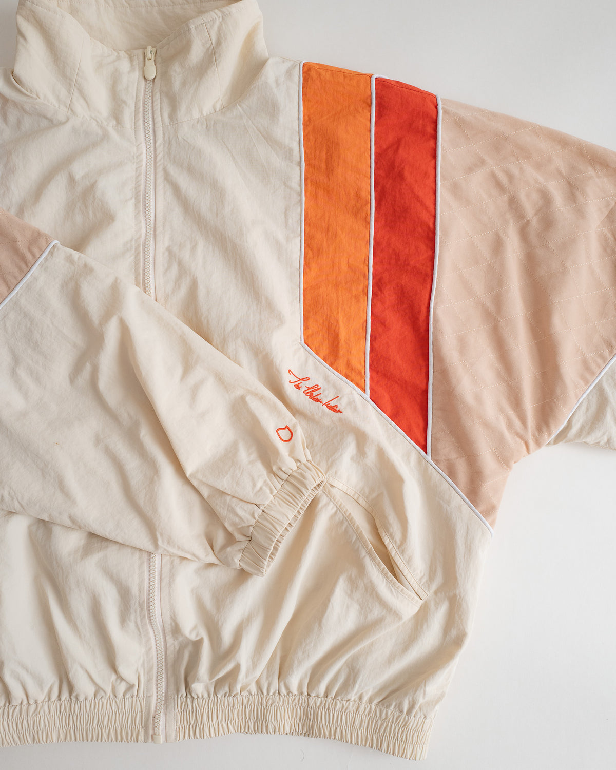 Close-up of the Saffron Orange stripes, piping and embroidered script on the Sweets Track Jacket #Color_Saffron Orange